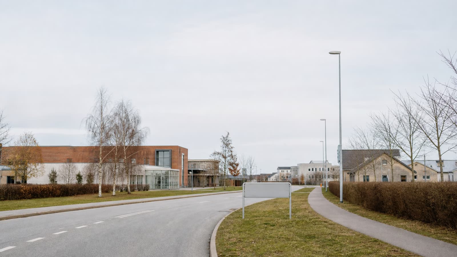 Kommunal bykant med vej, bygninger og et tomt byskilt i gråvejr