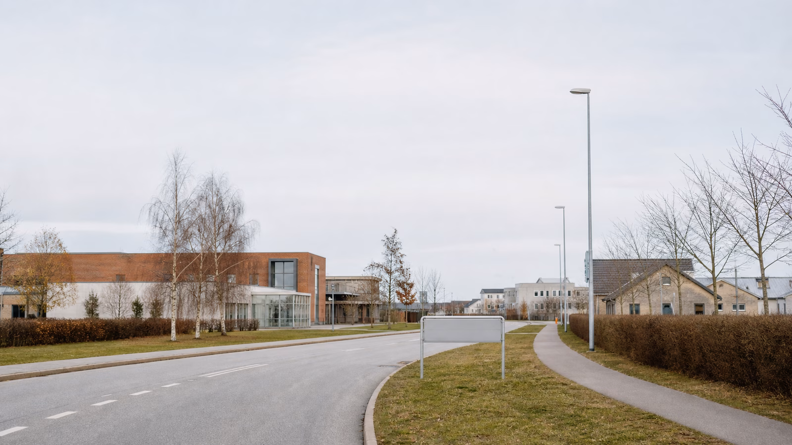 Kommunal bykant med vej, bygninger og et tomt byskilt i gråvejr